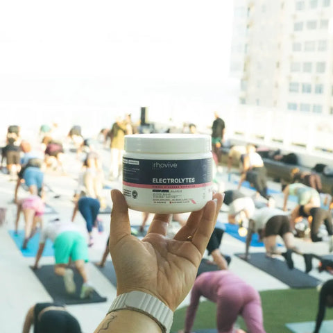 A hand holds up a jar of Rhovive Raspberry above a rooftop workout class