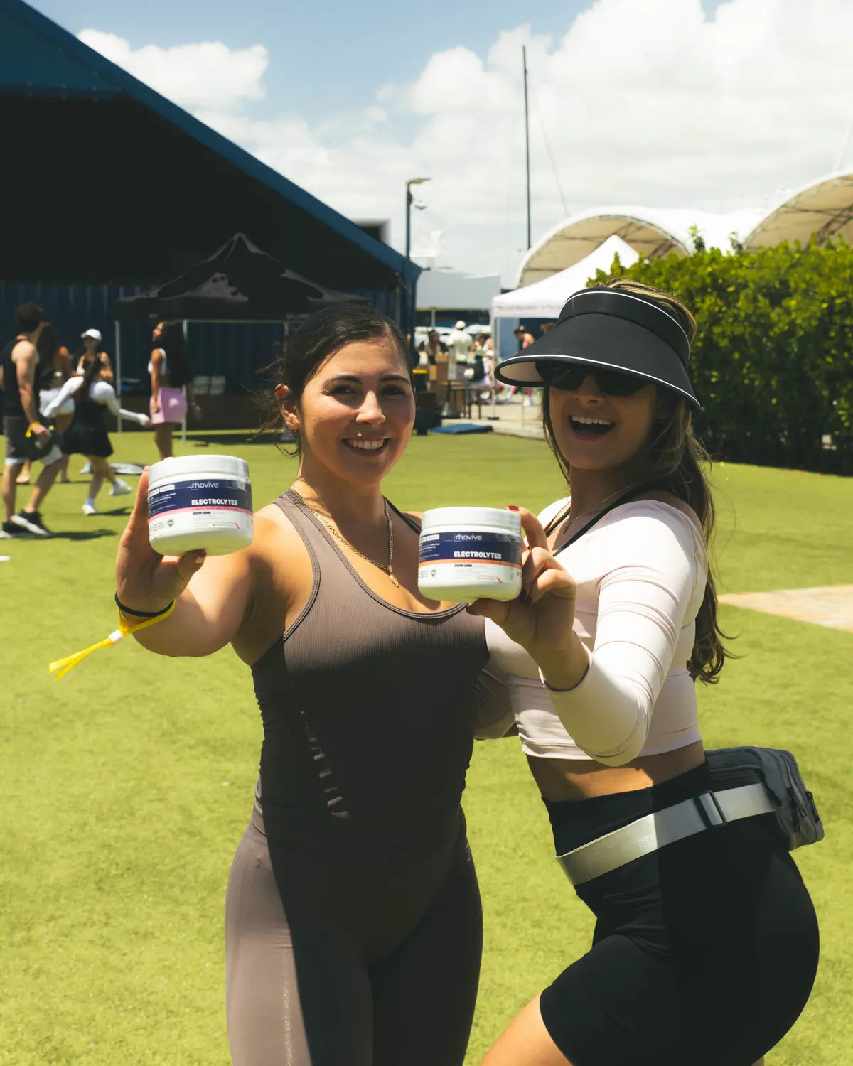 Two women at an outdoor fitness event holding up jars of Rhovive