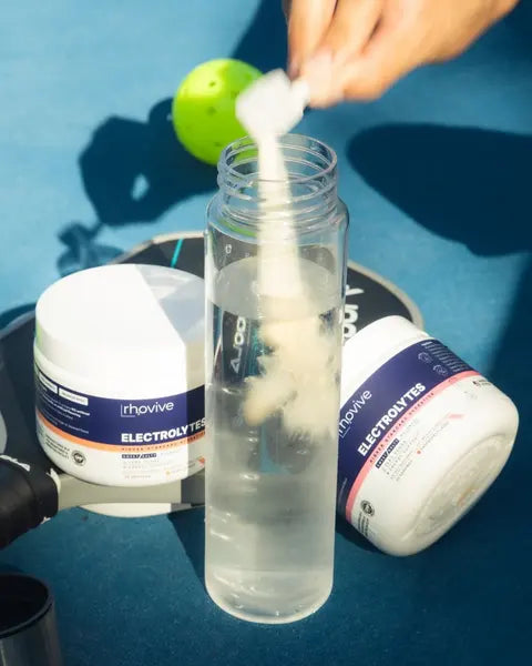 A scoop of Rhovive poured into a water bottle on a pickleball court