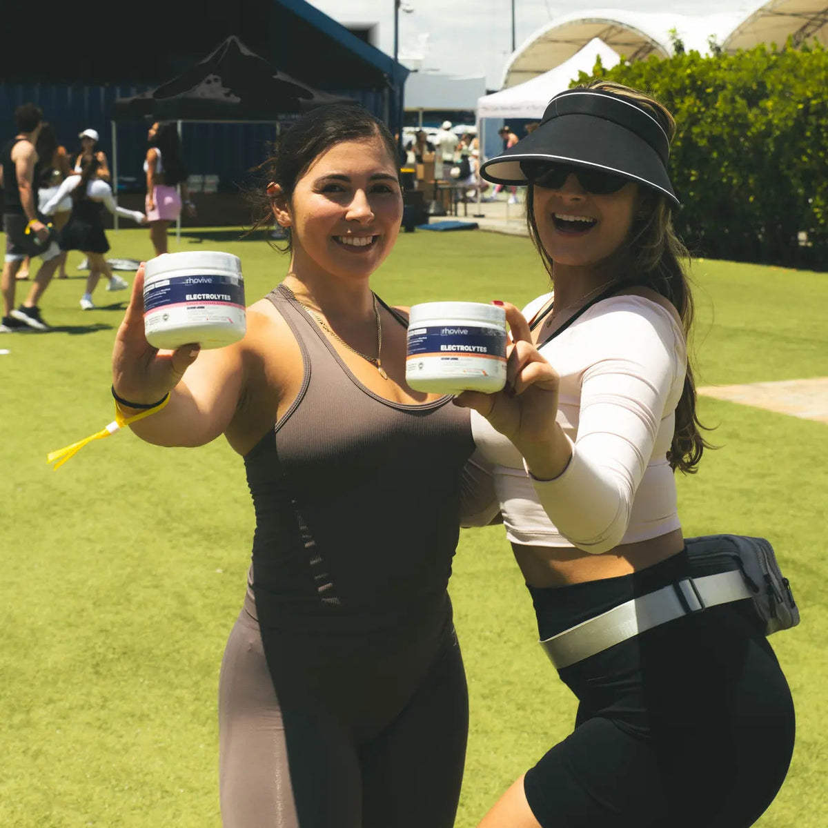 Two people at an outdoor event, each holding a jar of Rhovive, one Peach and one Raspberry