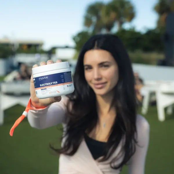 A woman at an outdoor event holds a jar of Rhovive Peach out toward the camera