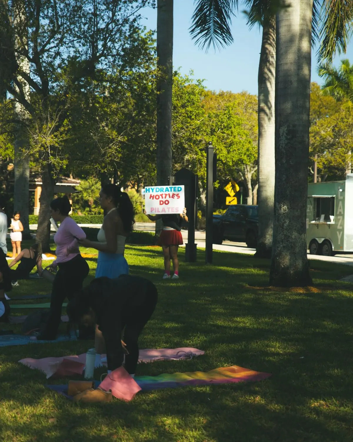A park pilates class; a sign reads: Hydrated hotties do pilates