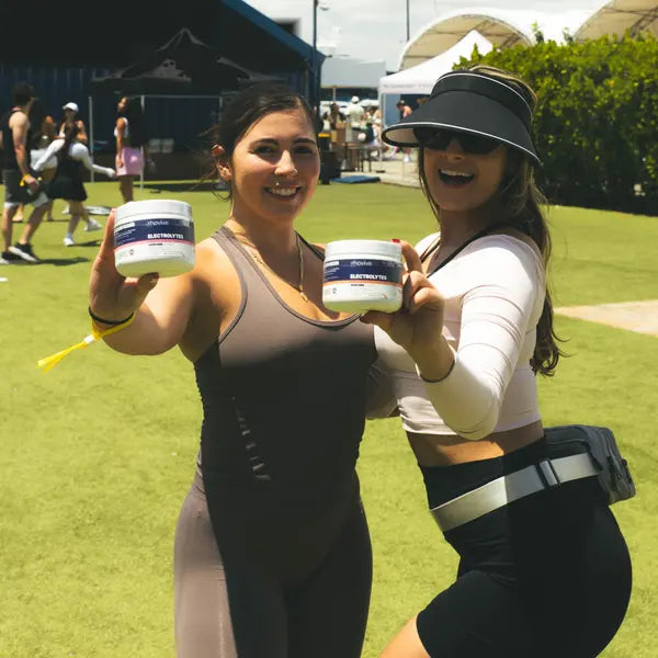 Two women at an outdoor fitness event holding up jars of Rhovive Raspberry and Peach